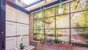 Een terras met een bakstenen muur, een houten tafel en plantenpotten.