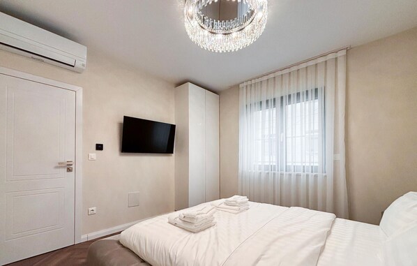 Una camera da letto moderna con un letto, una TV a schermo piatto, un lampadario e una finestra con tende.