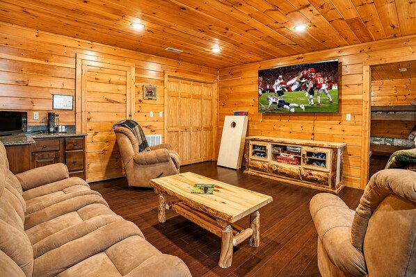 L’intérieur d’un chalet confortable, avec un plafond en bois, un téléviseur fixé au mur, une table basse en bois et des fauteuils moelleux.