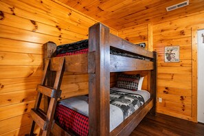 Un lit superposé avec une échelle, une couverture à carreaux rouges et noirs, et un oreiller à motifs.