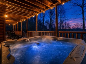 A hot tub area with a wooden deck and chairs, surrounded by a wooden railing, under a night sky. - Hot Tub, Pool Table, Fire Pit, Views / Smoky Mountain Cabin (Sevierville)