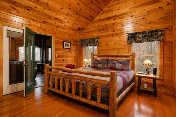A log cabin bedroom with a wooden bed, a nightstand, and a window with curtains. - Hot Tub, Pool Table, Fire Pit, Views / Smoky Mountain Cabin (Sevierville)