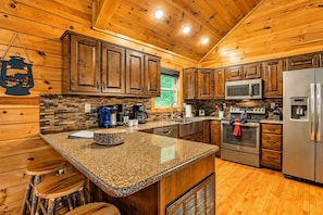 A kitchen with wooden cabinets, granite countertops, stainless steel appliances, and a hanging lantern. - Hot Tub, Pool Table, Fire Pit, Views / Smoky Mountain Cabin (Sevierville)