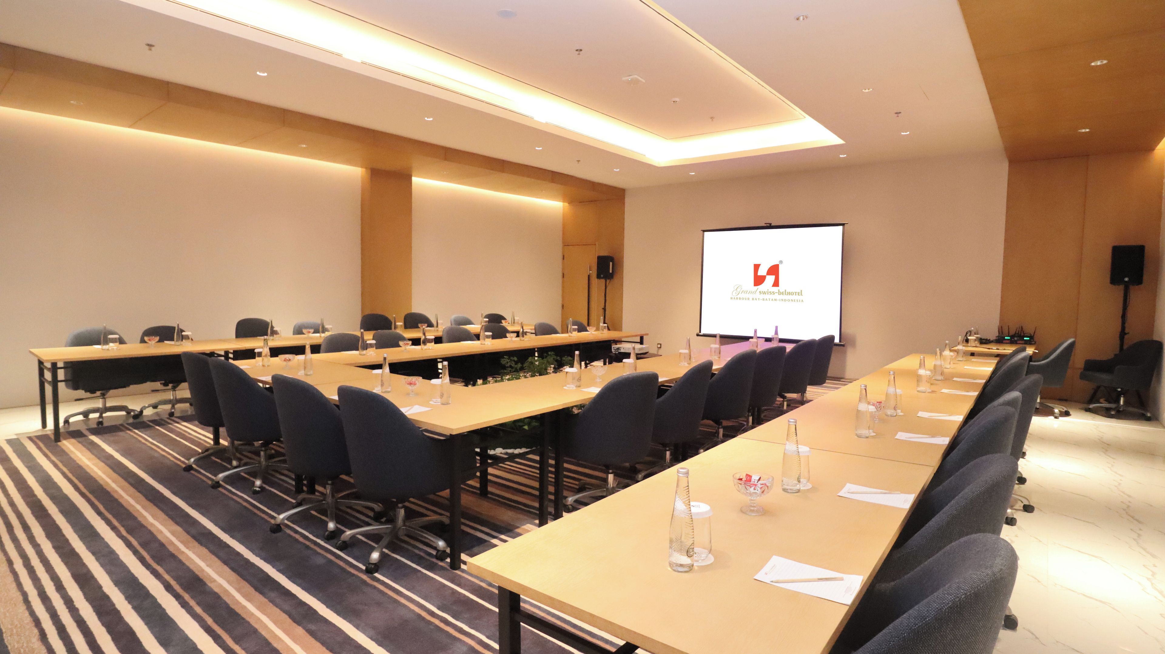A conference room with long tables, chairs, and a presentation screen.
