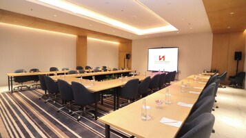 A conference room with long tables, chairs, and a presentation screen.