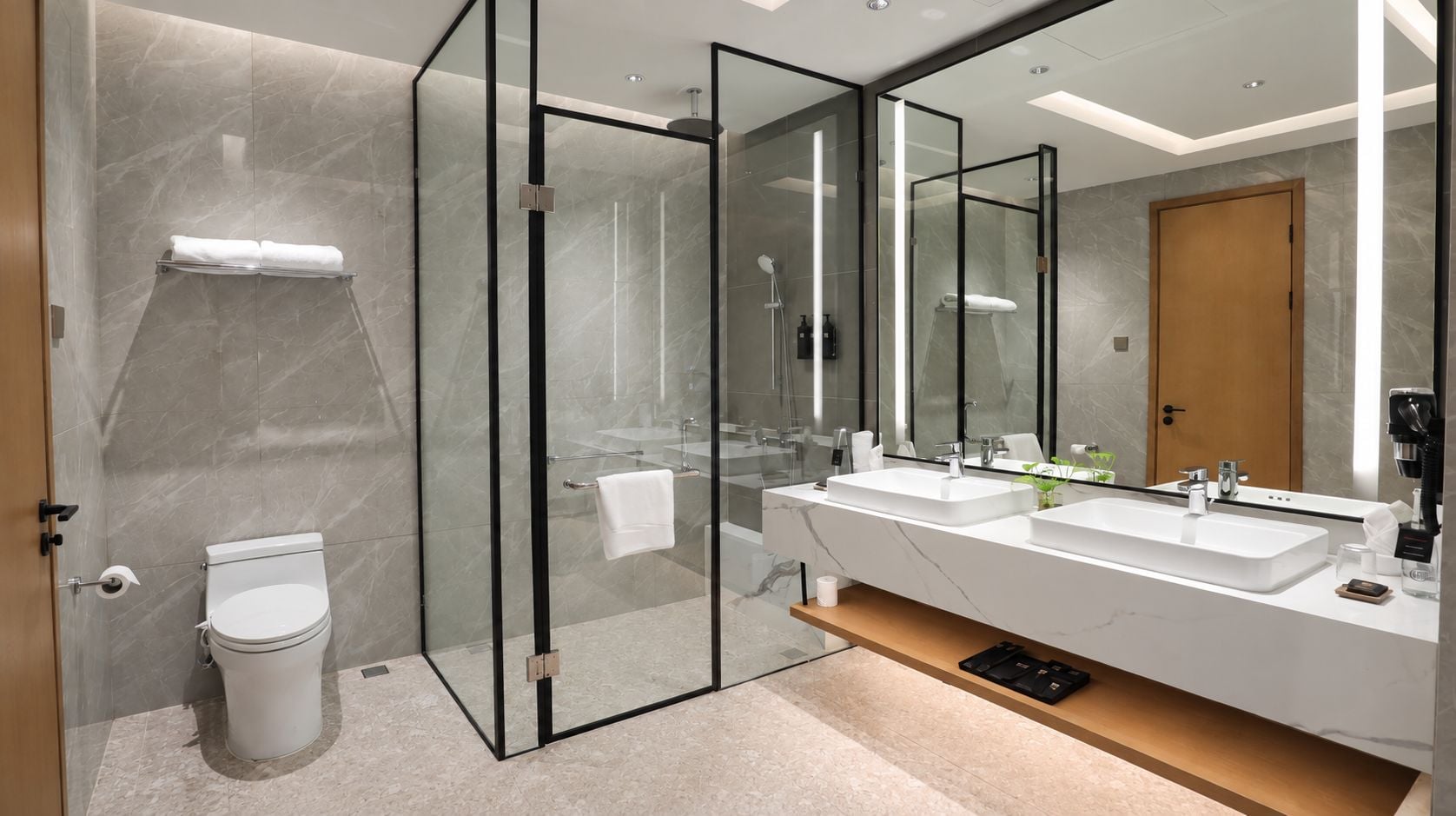 A modern bathroom with a glass-enclosed shower, a toilet, and a vanity with a large mirror.
