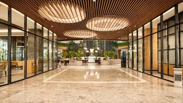 A spacious lobby with a marble floor, wooden ceiling panels, and a reception desk with plants.