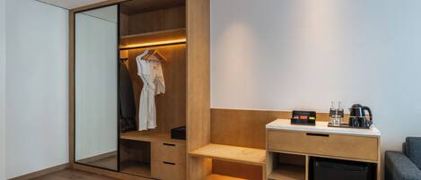 Una habitación de hotel moderna con vestidor, escritorio con cafetera y zona de estar.