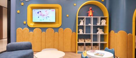 A children's play area with a TV, plush toys, and a bookshelf.