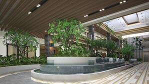 Un atrium intérieur moderne doté d’un élément aquatique central, de plusieurs niveaux de balcons et d’une végétation luxuriante.