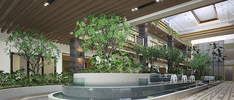 A modern indoor atrium with a central water feature, multiple levels of balconies, and lush greenery.