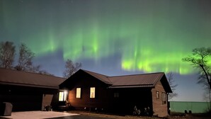 Eine zweistöckige Holzhütte mit Garage, unter einem Nachthimmel mit grünem Polarlicht.