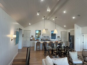 A spacious kitchen with white wooden paneling, a large island with bar stools, and pendant lighting.