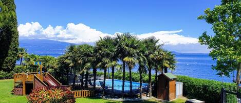 Zona de piscina con tobogán, rodeada de palmeras y vista al mar.