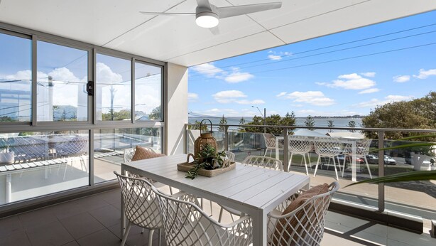 A balcony with a table and chairs, a decorative lantern, and a view of the water and city skyline.