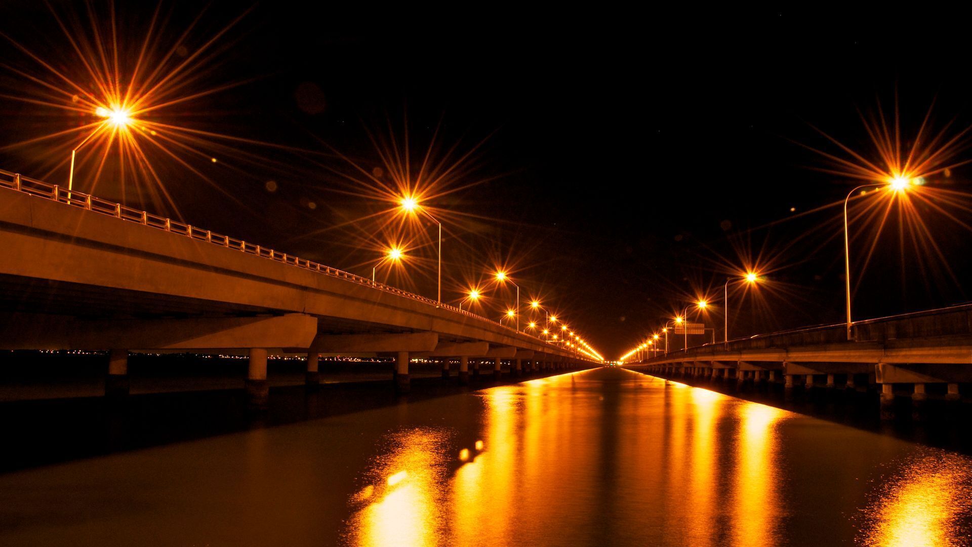 Vista nocturna de un puente con luces de la calle reflejándose en el agua.