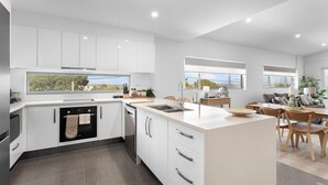 A modern kitchen with white cabinetry, a built-in oven, and a large window overlooking greenery.