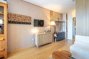 Un salon moderne avec un plancher en bois, un téléviseur à écran plat fixé au mur, un meuble en bois, une lampe et un canapé.