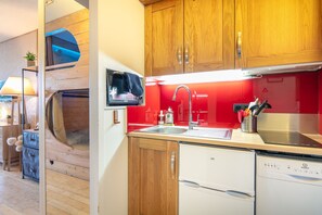 A compact kitchen with wooden cabinets, a built-in microwave, a sink, and a dishwasher. - Zen Altitude- Piscine partagée (Chamrousse)