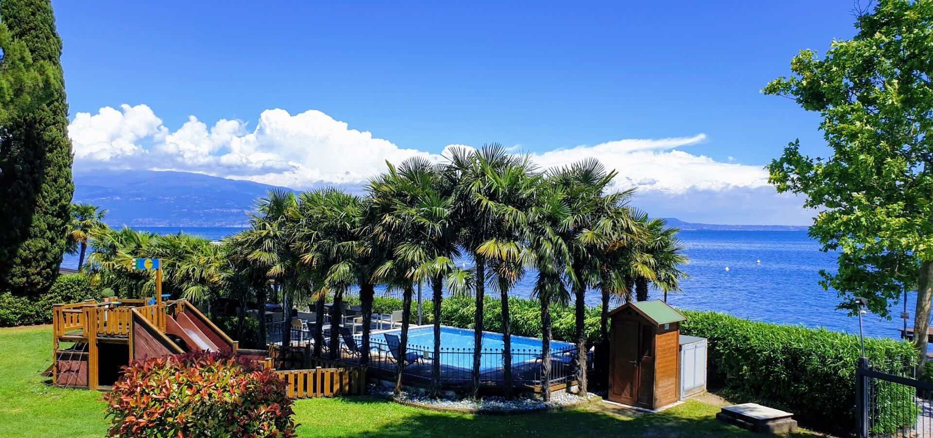 Ein Poolbereich mit Rutsche, umgeben von Palmen und Blick aufs Meer.
