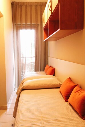 Een hotelkamer met een bed, oranje kussens, een hoofdbord en een raam met gordijnen.