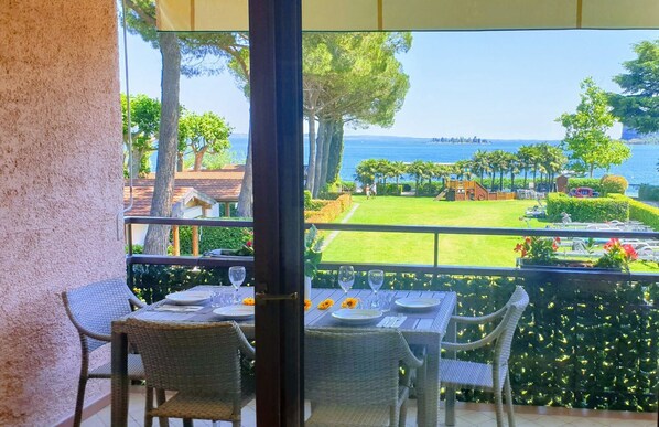 A balcony with a table set for two, overlooking a well-maintained lawn and a view of the sea. - Bianca Three-Room Apartment with lake view. (San Felice del Benaco)