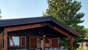 Eine moderne Holzblockhütte mit überdachter Terrasse, Sitzgelegenheiten im Freien und einem gepflegten Rasen.
