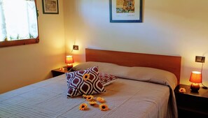 Ein ordentlich bezogenes Bett mit gemusterten Kissen, ein Nachttisch mit Lampe und ein gerahmtes Bild an der Wand.