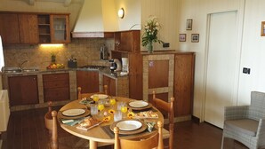 Une cuisine chaleureuse avec des meubles en bois, une table à manger dressée pour le petit-déjeuner et une chaise en osier.