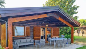 Ein überdachter Außenbereich mit Holzterrasse, einer Couch und einem Tisch mit Stühlen.