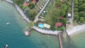 Eine Vogelperspektive zeigt eine Küstenlandschaft mit einem Hafen, einem Schwimmbad und mehreren Gebäuden mit roten Dächern.
