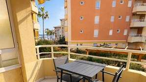 Ein Balkon mit Tisch und Stühlen, einem gelben Geländer und Blick auf ein mehrstöckiges Gebäude mit Balkonen.