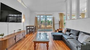 A modern living room with a wooden coffee table, grey sofa, and a TV mounted on the wall.