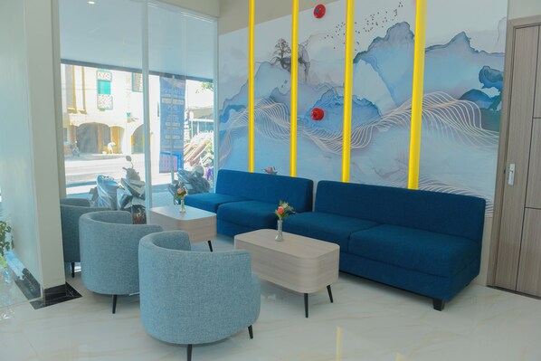 Un vestíbulo moderno con un sofá azul, dos sillones grises, una mesita de centro y un mural decorativo.