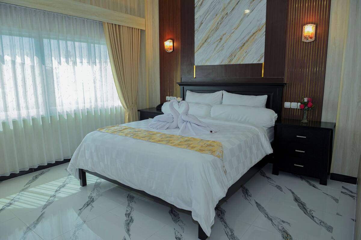 Habitación de hotel con una cama grande, una mesita de noche, una lámpara de pared y piso con estampado de mármol.