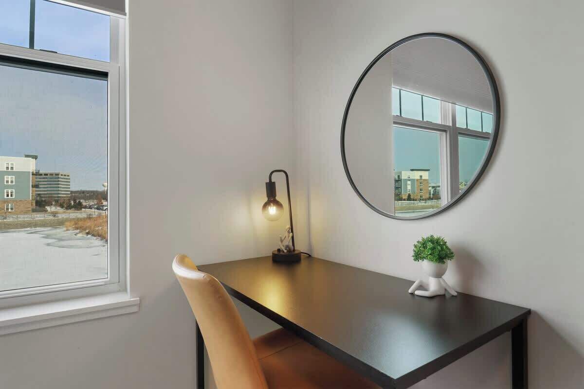 Une pièce comprenant un bureau, une chaise, un miroir rond et une petite plante en pot.