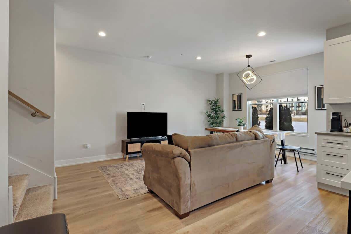 Un salon moderne avec un canapé beige, un téléviseur à écran plat et un coin repas comprenant une table et des chaises.