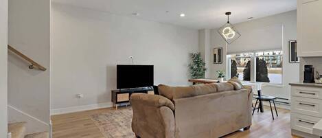 Un salon moderne avec un canapé beige, un téléviseur à écran plat et un coin repas comprenant une table et des chaises.