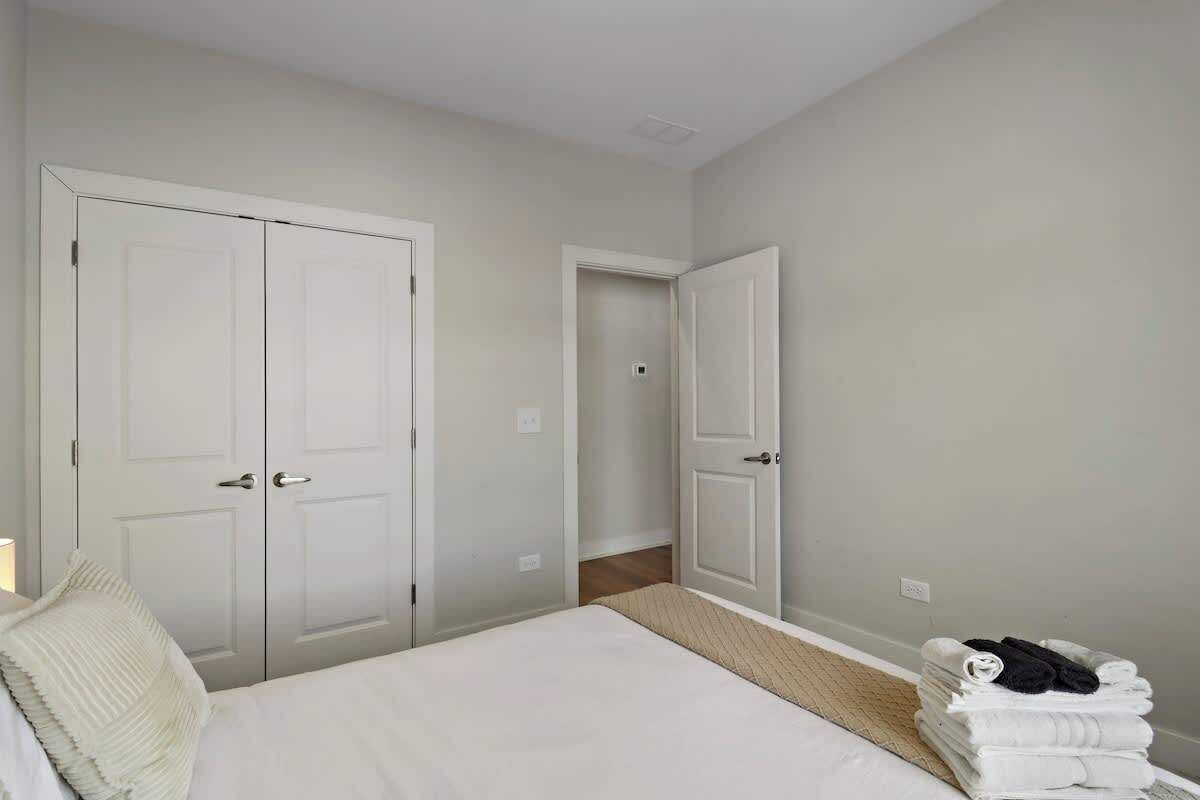 A bedroom with a bed, two white doors, a small stack of towels, and a light switch on the wall.