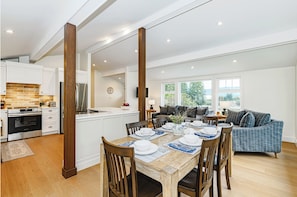 A modern kitchen with white cabinets, a stainless steel refrigerator, and a wooden dining table set for four.