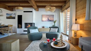A modern living room with a fireplace, two armchairs, a coffee table, and a dining area with a wooden table and chairs.