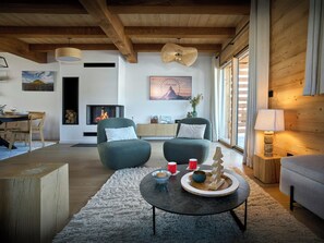 Ein modernes Wohnzimmer mit Kamin, zwei Sesseln, einem Couchtisch und einem Essbereich mit Holztisch und Stühlen.