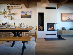 Ein moderner Essbereich mit einem Holztisch, der für eine Mahlzeit gedeckt ist, einem Kamin mit Holz und einem aufgehängten Bild von einem Berg.
