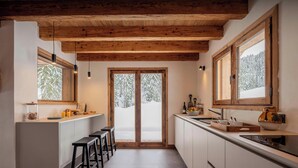 A modern kitchen with wooden beams, a large window, and a view of a snowy landscape. - Chalet Amethyste - Garden and swim spa in Saint-Gervais - OVO Network (Saint-Gervais-les-Bains)