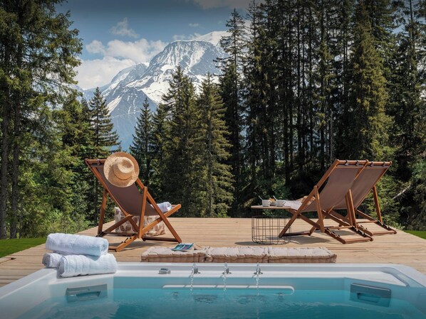 A pool area with lounge chairs, a hat, towels, and a deck overlooking a forest and mountains. - Chalet Amethyste - Garden and swim spa in Saint-Gervais - OVO Network (Saint-Gervais-les-Bains)