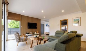 Ein modernes Wohnzimmer mit einer Couch, einem gemusterten Sessel, einem kleinen runden Tisch und einem an der Wand befestigten Fernseher.
