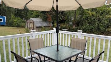 A deck with a glass-top table and four chairs, surrounded by a white fence.