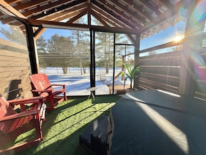 A covered patio with a view of a snowy landscape, a wooden pergola, and a red chair.