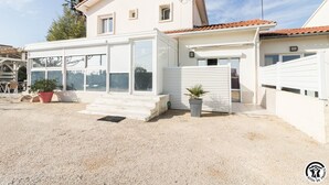 Ein zweistöckiges Haus mit weißer Fassade, einem Ziegeldach und einer überdachten Terrasse.
