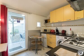 Una cocina compacta con armarios amarillos, una estufa a gas, microondas, lavadora y un pequeño comedor con mesa y sillas.